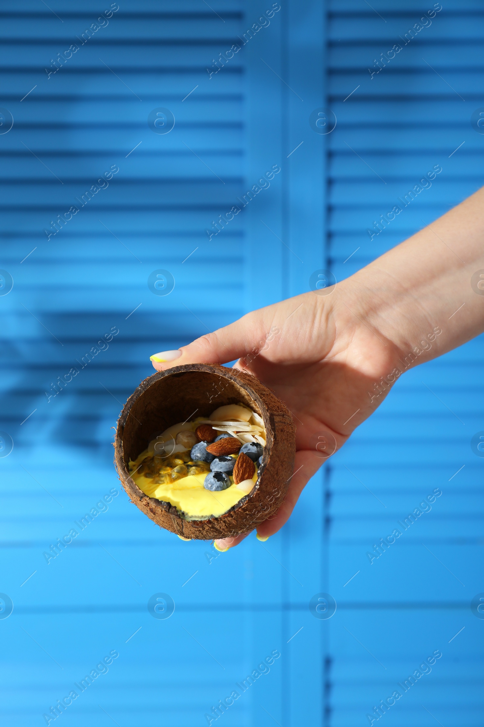 Photo of Woman holding coconut shell with tasty smoothie bowl on blurred background, closeup