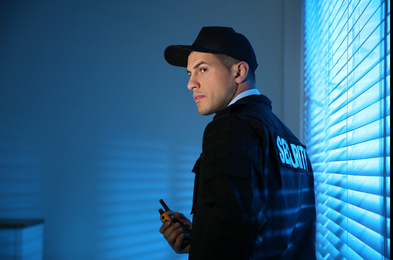 Photo of Professional security guard with portable radio set near window in dark room