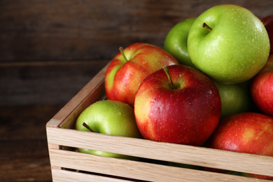 Ripe juicy apples in wooden crate on wooden table, closeup