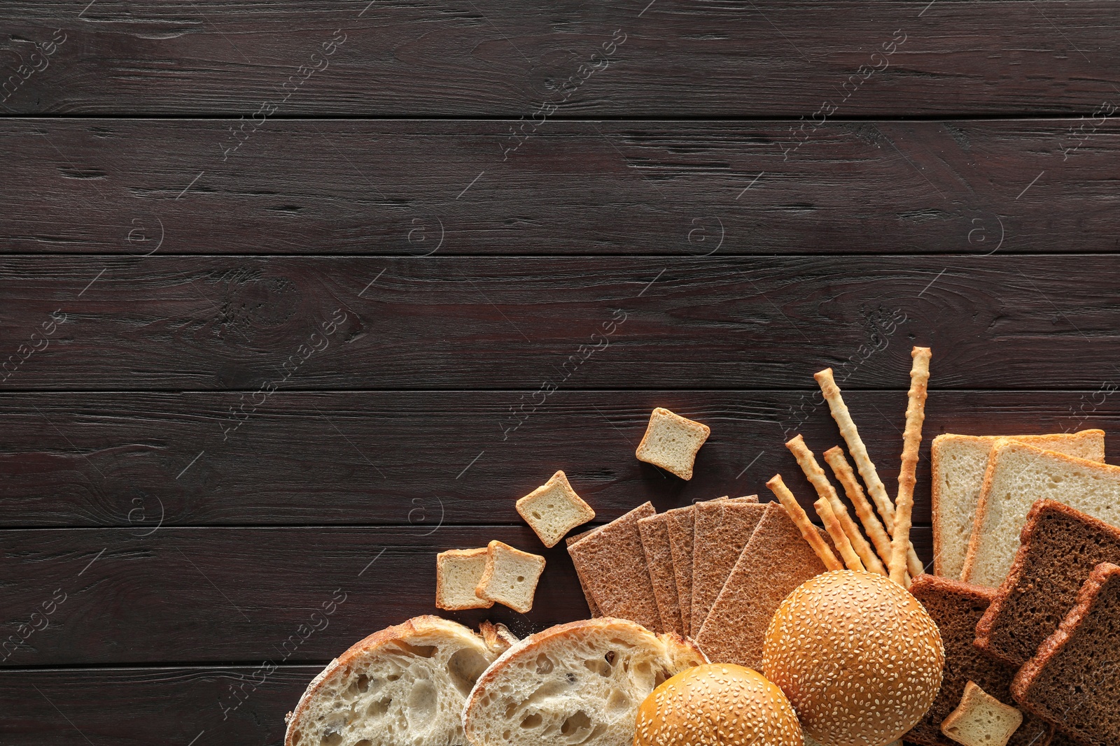 Photo of Food photography. Delicious bread slices and different bakery products on black wooden table, flat lay with space for text
