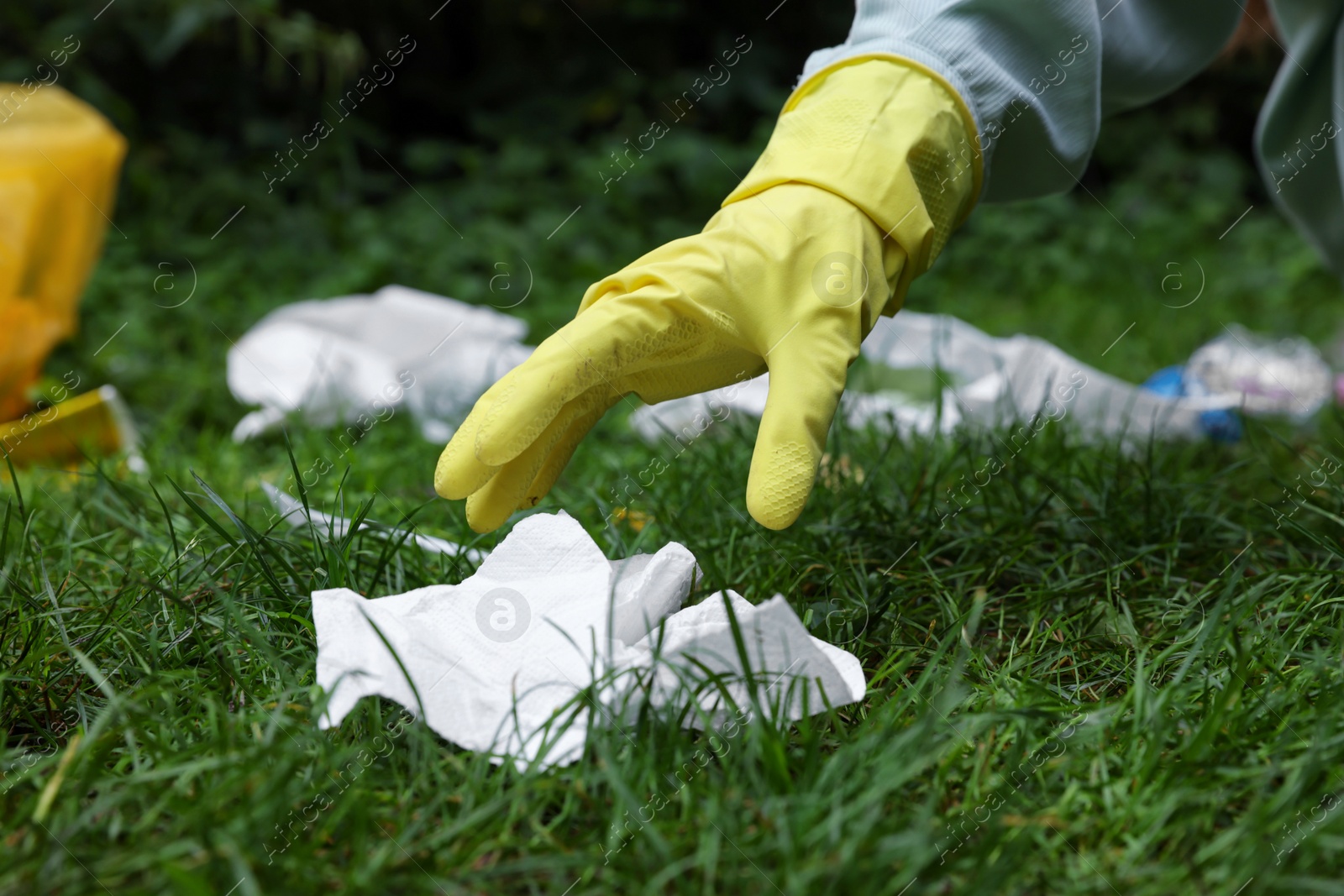 Photo of Woman collecting garbage on green grass, closeup