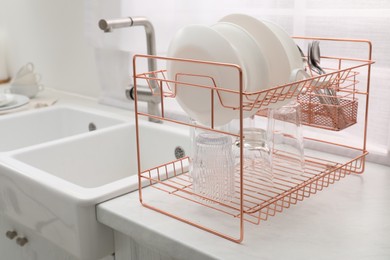 Drying rack with clean dishes on light marble countertop near sink in kitchen