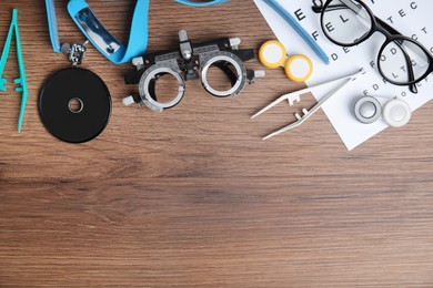 Different ophthalmologist tools on wooden background, flat lay. Space for text