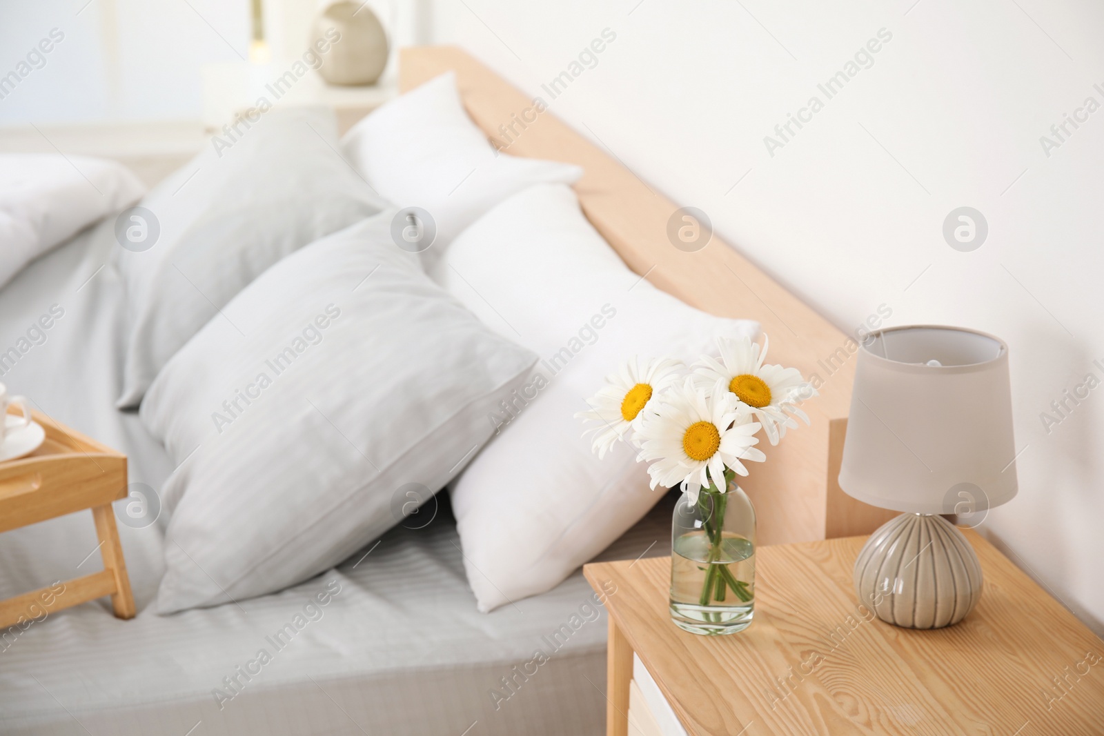 Photo of Bouquet of beautiful daisy flowers and lamp on nightstand in bedroom, space for text