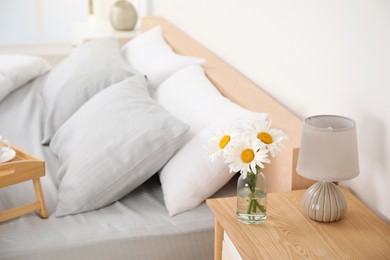 Bouquet of beautiful daisy flowers and lamp on nightstand in bedroom, space for text