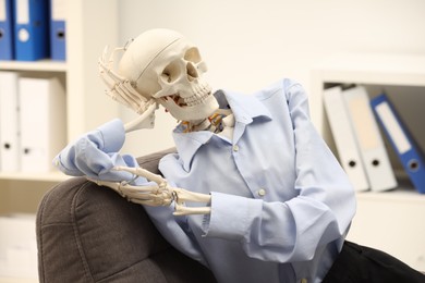 Waiting concept. Human skeleton sitting in armchair at office