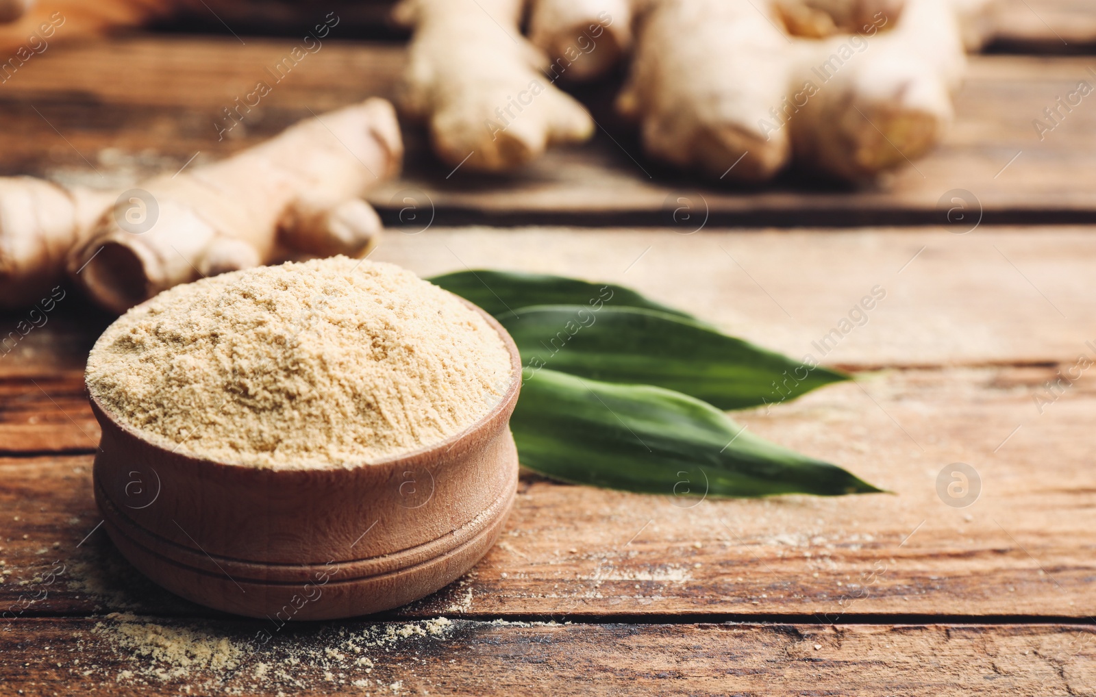 Photo of Dry ginger powder, fresh root and leaves on wooden table. Space for text