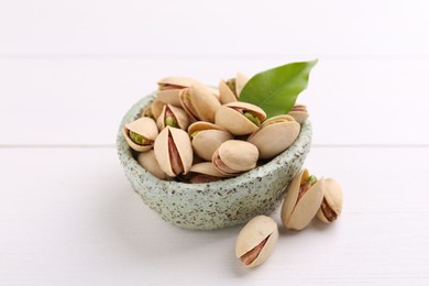 Delicious pistachios in bowl on white table