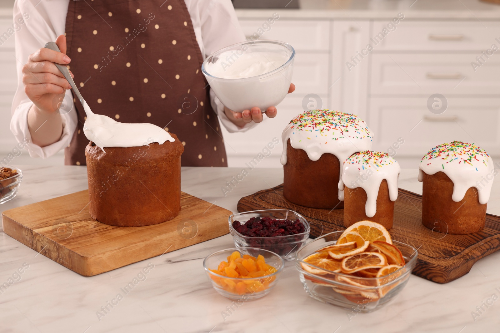 Photo of Woman decorating traditional Easter cake with glaze at white marble table in kitchen, closeup