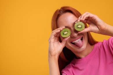 Funny woman covering eyes with halves of fresh kiwi and showing tongue on orange background, space for text