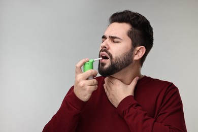 Photo of Young man using throat spray on grey background