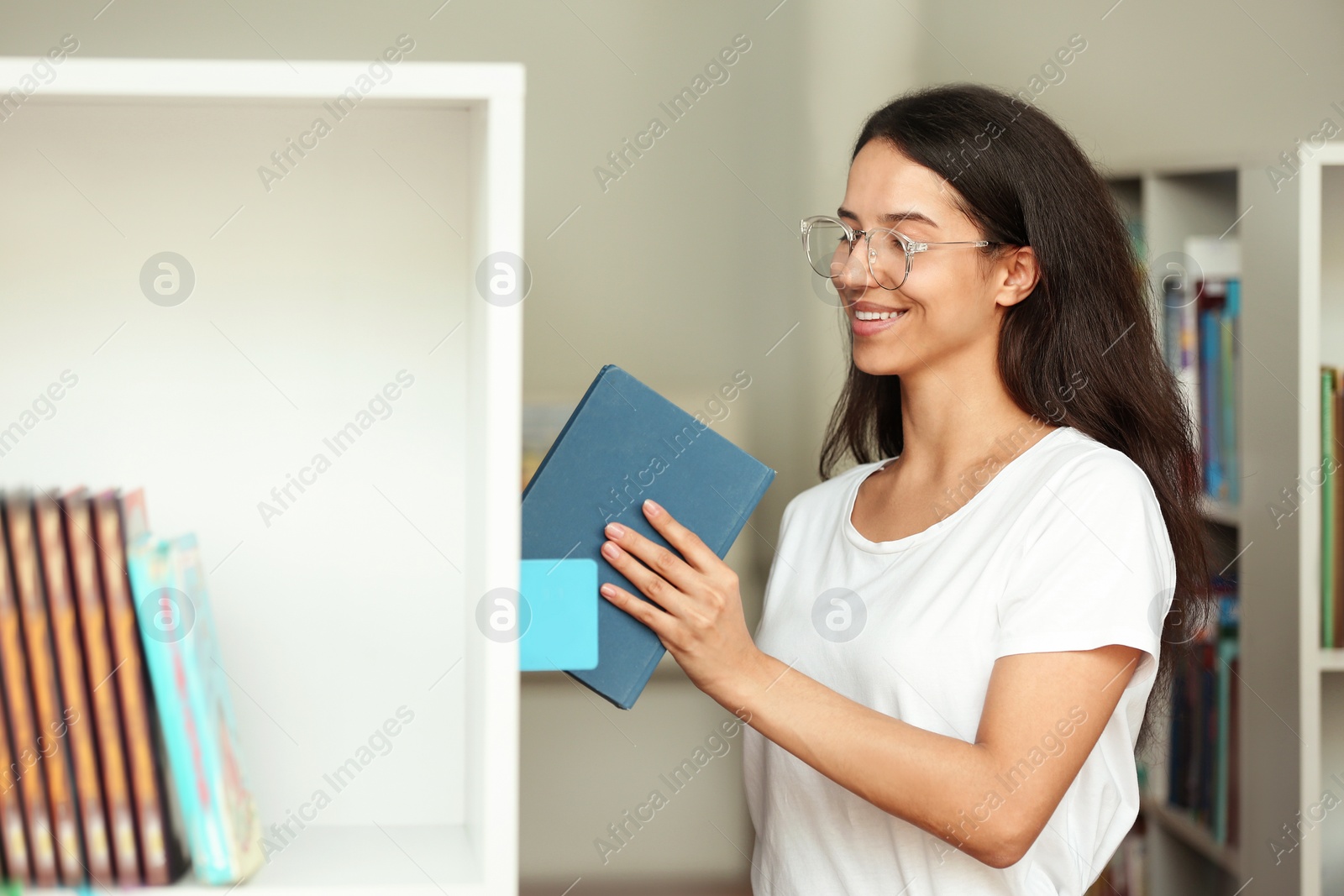 Photo of Young woman putting book on shelf in library