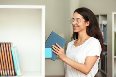 Young woman putting book on shelf in library