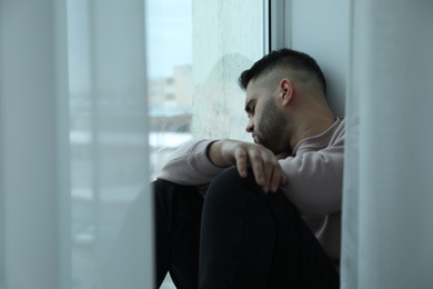 Sad man sitting near window at home