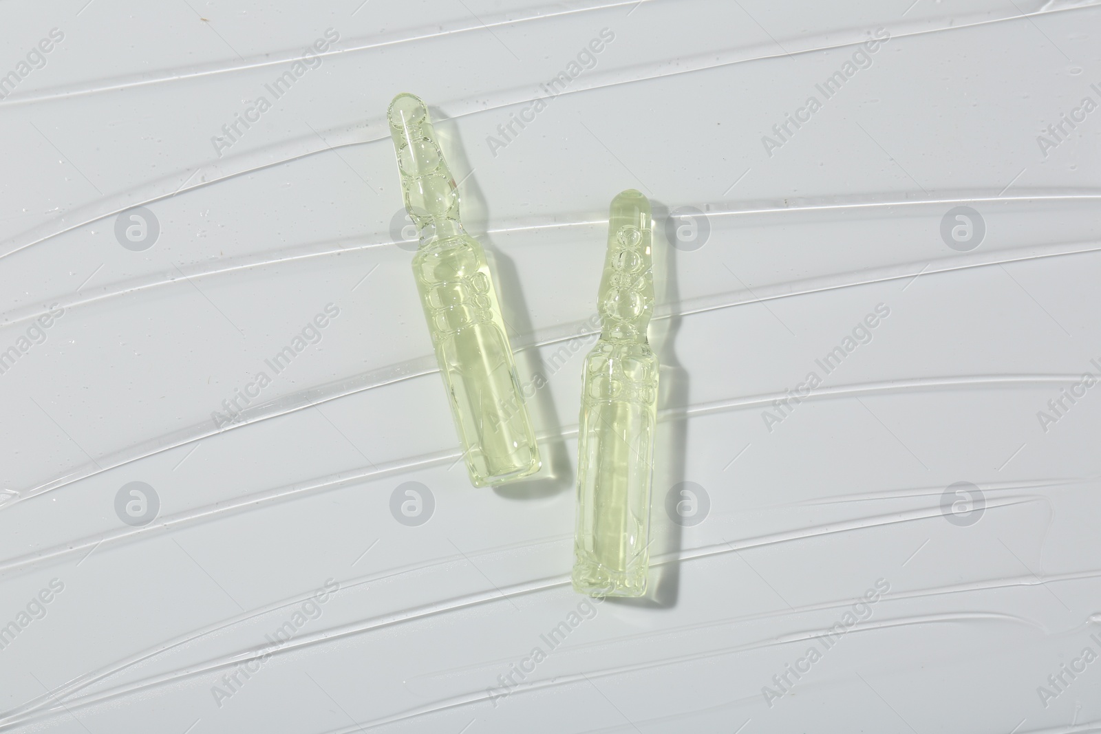 Photo of Skincare ampoules on white surface covered with gel, top view