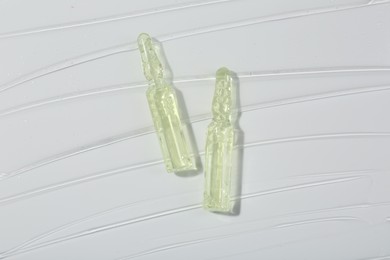 Photo of Skincare ampoules on white surface covered with gel, top view