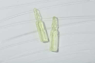 Skincare ampoules on white surface covered with gel, top view