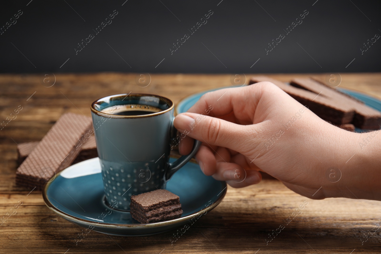 Photo of Woman with cup of delicious coffee and wafers at wooden table, closeup