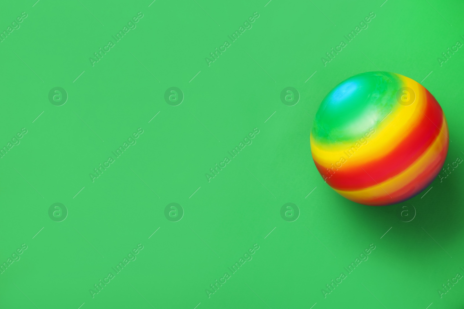 Photo of Bright rubber kids' ball on green background, top view. Space for text