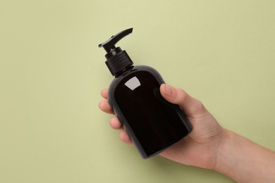 Photo of Woman holding shampoo bottle on olive background, top view