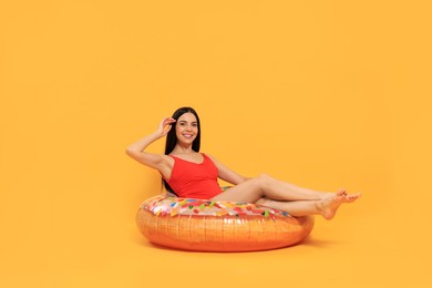 Photo of Happy young woman with beautiful suntan sitting on inflatable ring against orange background