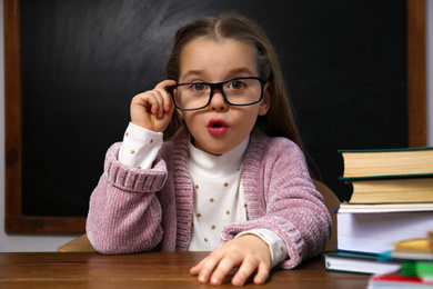 Photo of Cute little child wearing glasses at desk in classroom. First time at school