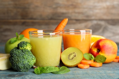 Photo of Glasses of delicious juices and fresh ingredients on blue wooden table