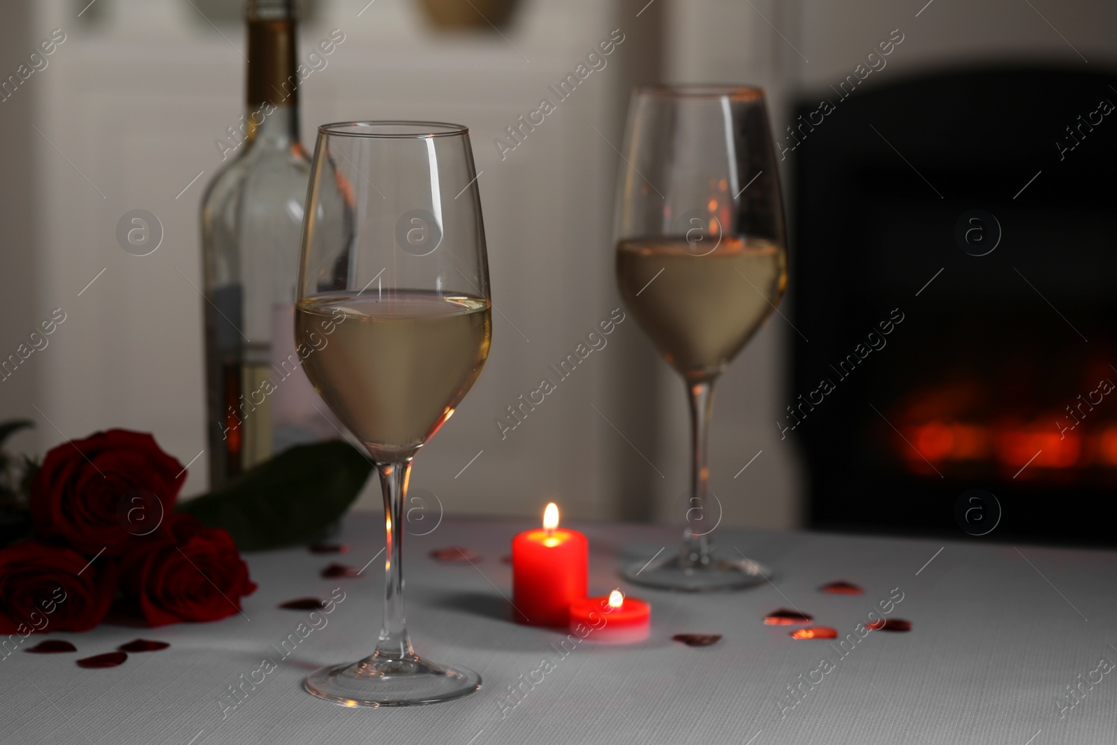 Photo of Glasses of white wine, rose flowers and burning candles on grey table against blurred background. Romantic atmosphere