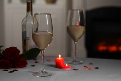 Glasses of white wine, rose flowers and burning candles on grey table against blurred background. Romantic atmosphere