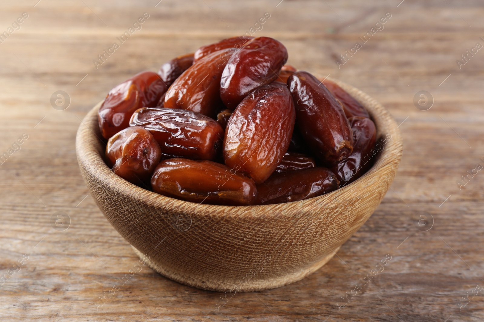 Photo of Sweet dried dates in bowl on wooden table, closeup