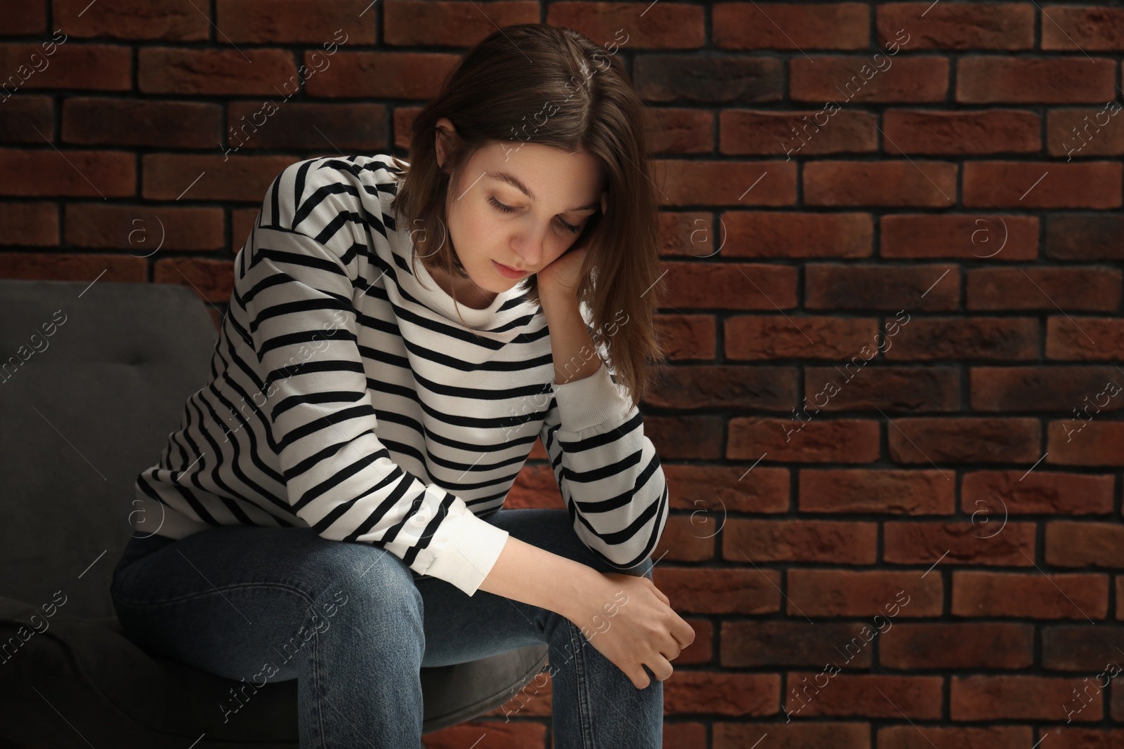 Photo of Sad young woman sitting on chair near brick wall, space for text