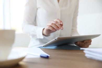 Photo of Businesswoman working with modern tablet at wooden table in office, closeup