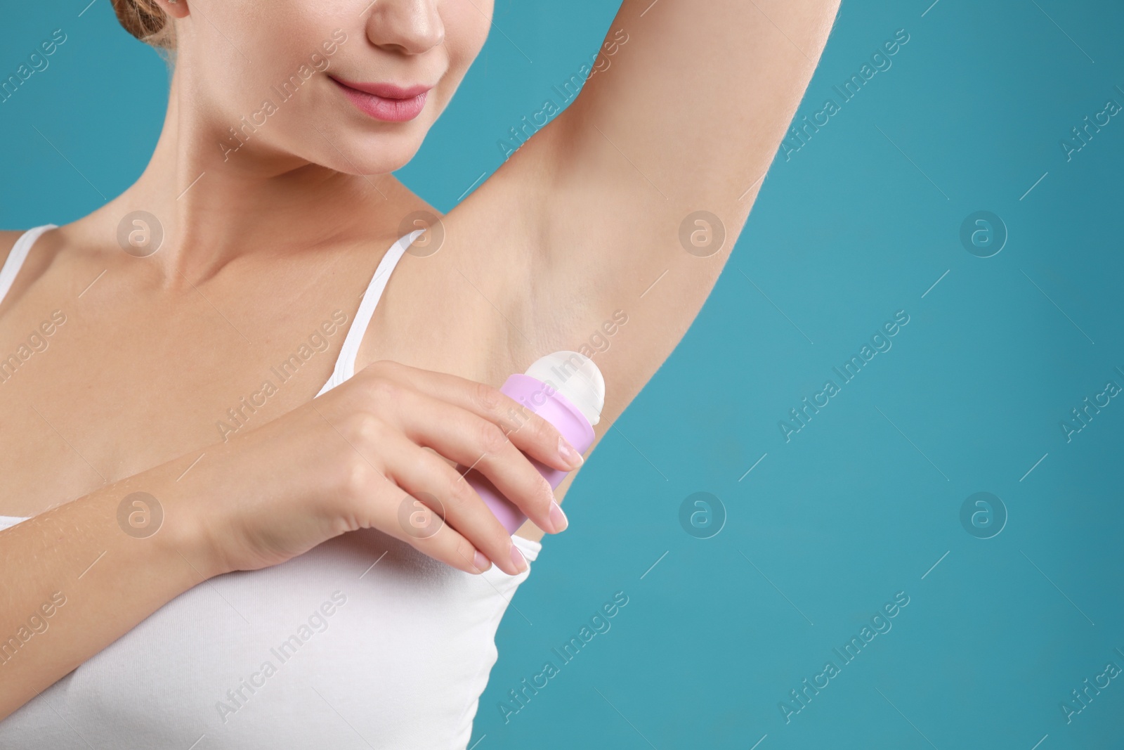 Photo of Young woman applying deodorant to armpit on teal background, closeup. Space for text