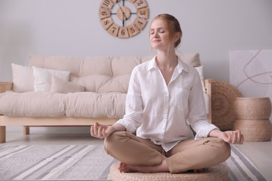 Woman meditating on wicker mat at home