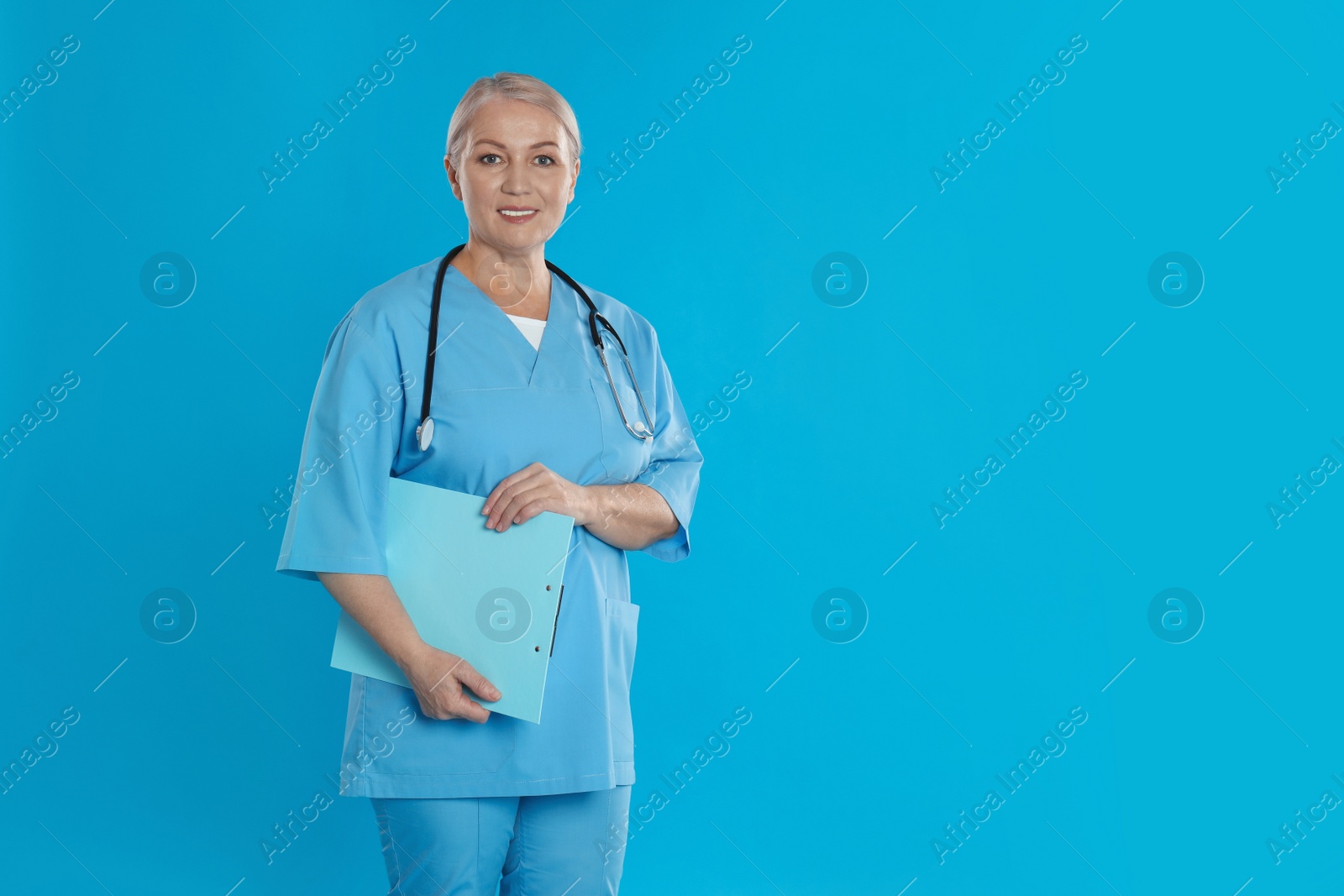 Photo of Mature doctor with stethoscope and clipboard on blue background. Space for text