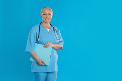 Mature doctor with stethoscope and clipboard on blue background. Space for text