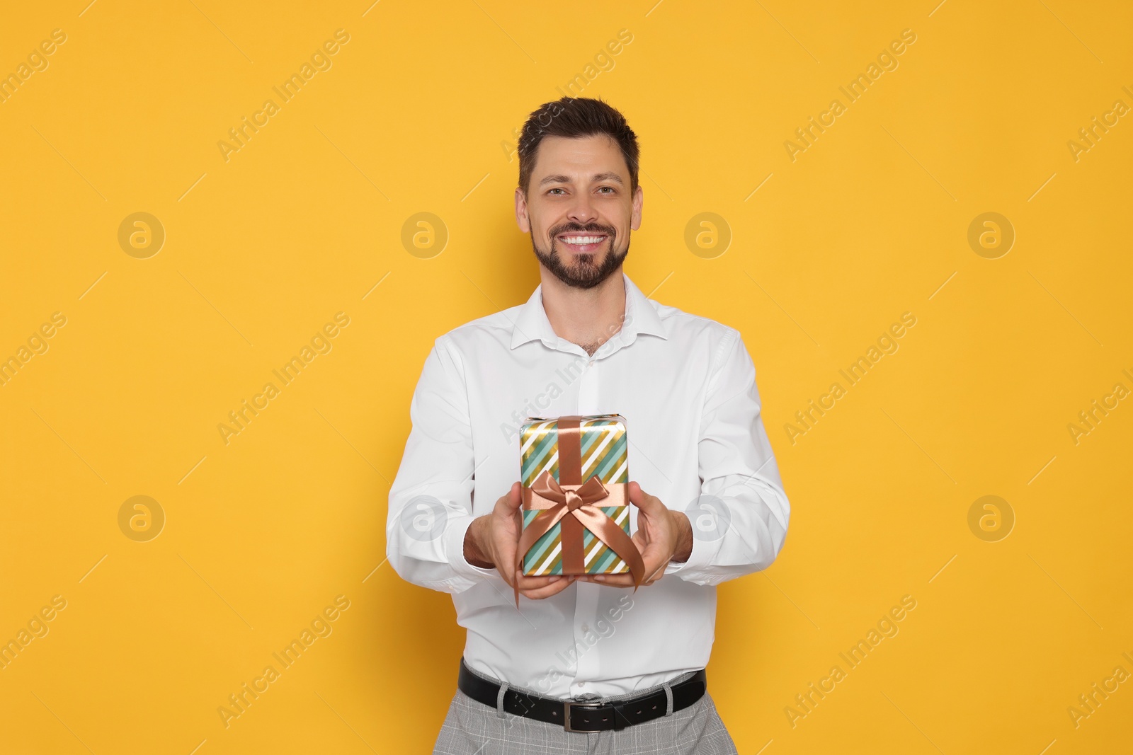 Photo of Happy man with gift box on yellow background