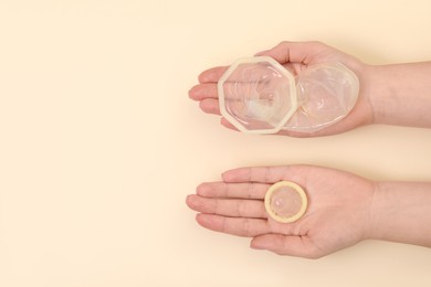 Photo of Woman with unrolled female and male condoms on beige background, top view. Space for text