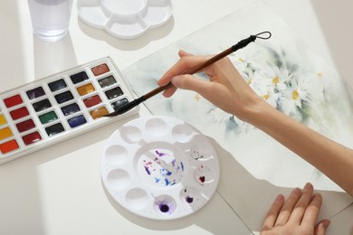 Photo of Woman painting flowers with watercolor at white table, above view. Creative artwork