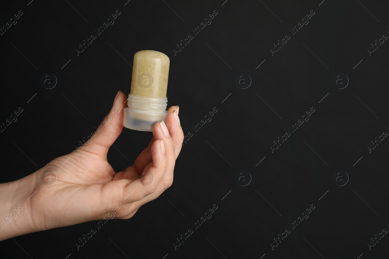 Photo of Young woman holding natural crystal alum deodorant on black background, closeup. Space for text