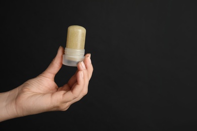 Photo of Young woman holding natural crystal alum deodorant on black background, closeup. Space for text