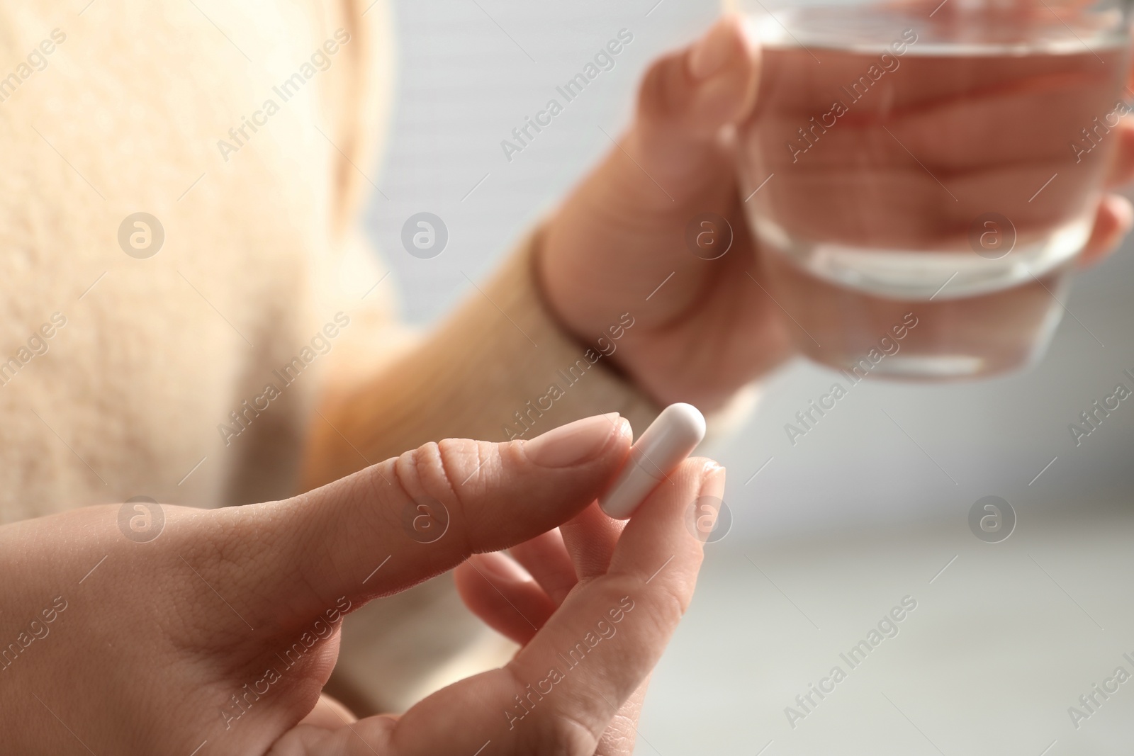 Photo of Woman with pill and glass of water on blurred background, closeup