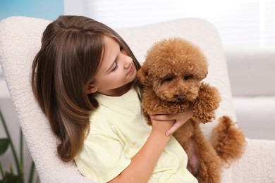 Photo of Little child with cute puppy in armchair at home. Lovely pet