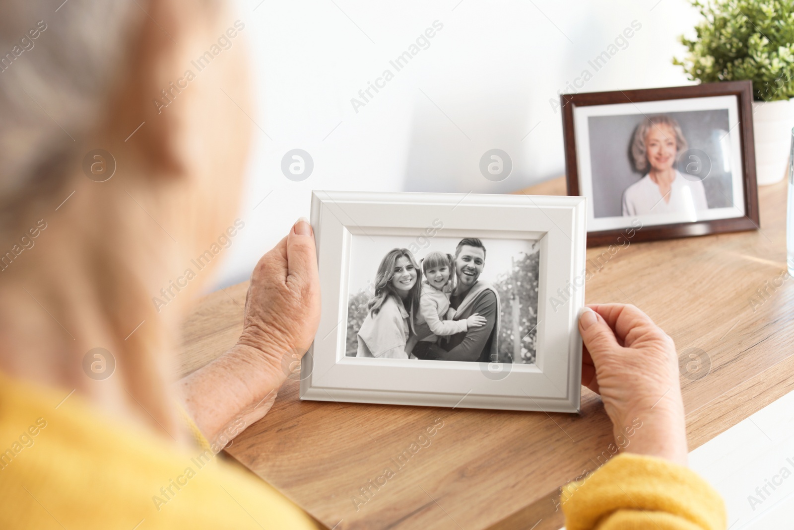 Photo of Elderly woman with framed family portrait at home