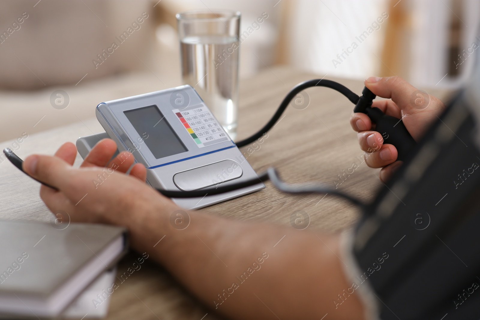 Photo of Man checking blood pressure at wooden table indoors, closeup