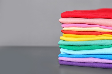 Photo of Stack of colorful t-shirts on table against gray background