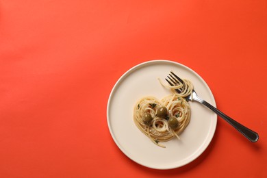 Photo of Heart made of tasty spaghetti, fork, olives and cheese on coral background, top view. Space for text