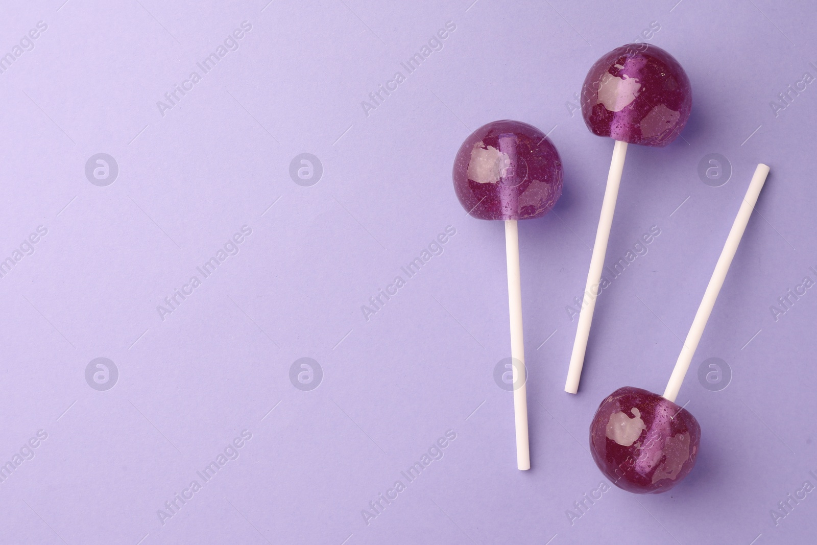 Photo of Tasty lollipops on violet background, flat lay. Space for text