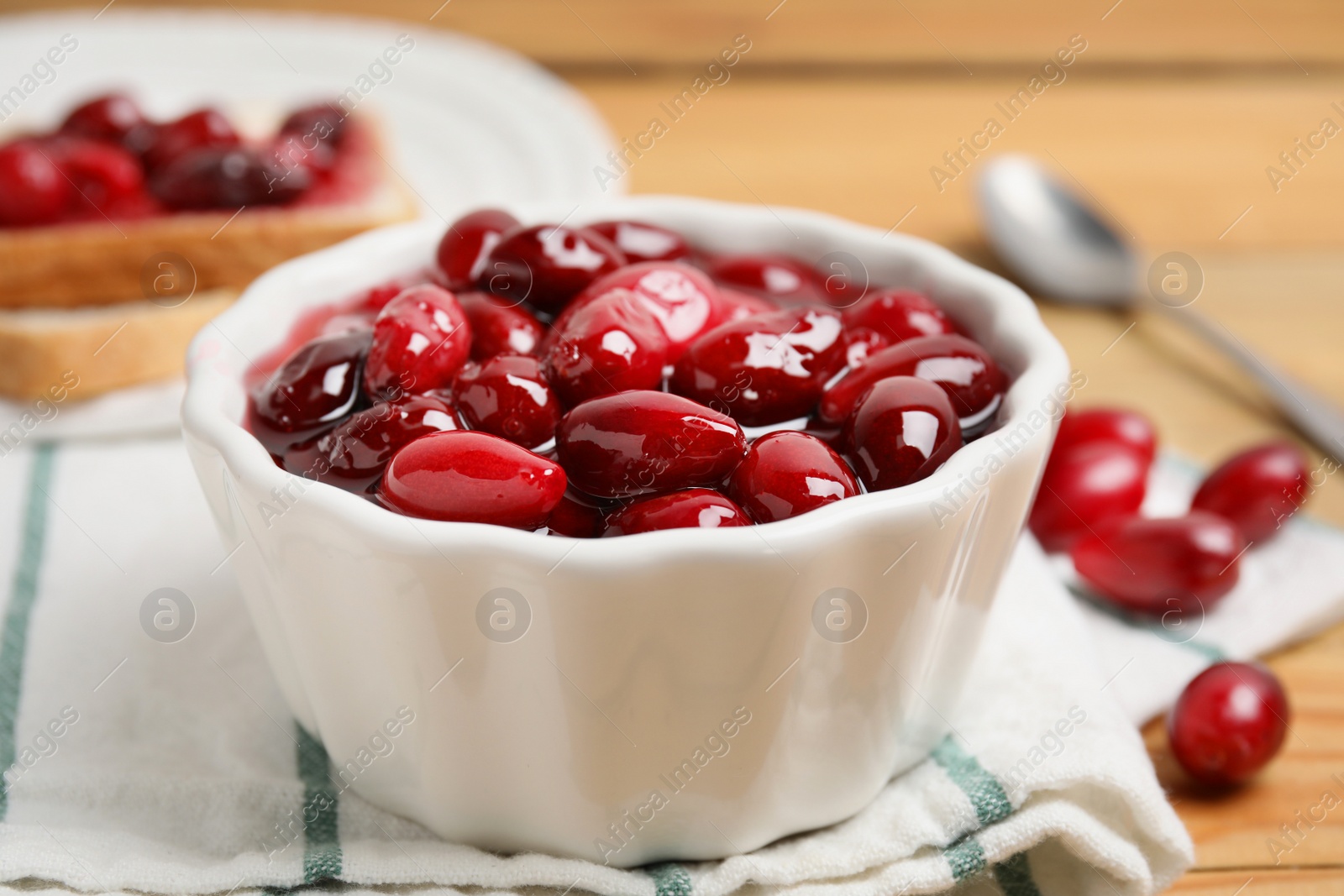 Photo of Delicious dogwood jam with berries in bowl on table, closeup