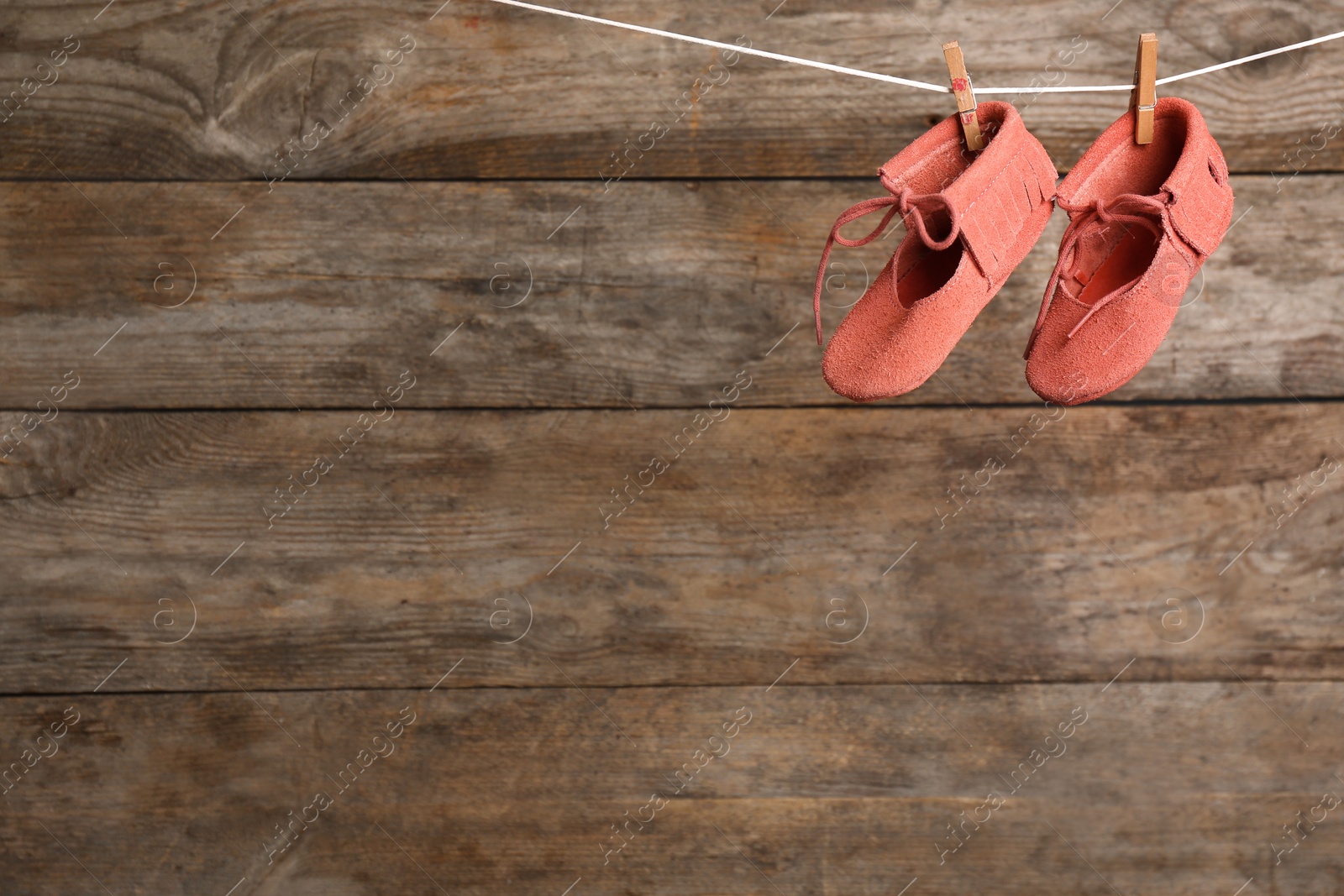 Photo of Pair of shoes on laundry line against wooden background, space for text. Baby accessories